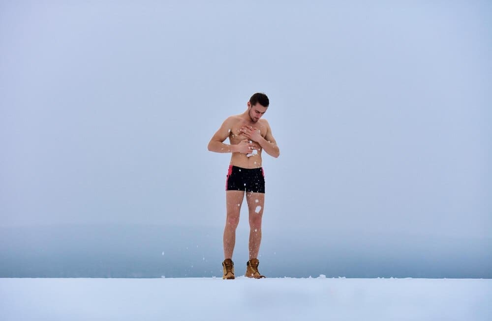 A shirtless man stands in the snow, presumably for a winter health practice.