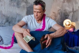 A mature man with a displeased expression holds a wallet and looks away.