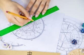 A woman with glasses draws a natal chart, with a selective focus on her hands and the chart.