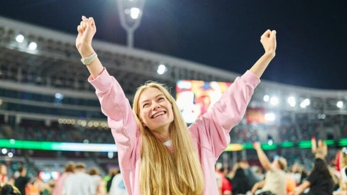 A woman sits in a stadium, watching a match broadcast on her laptop.