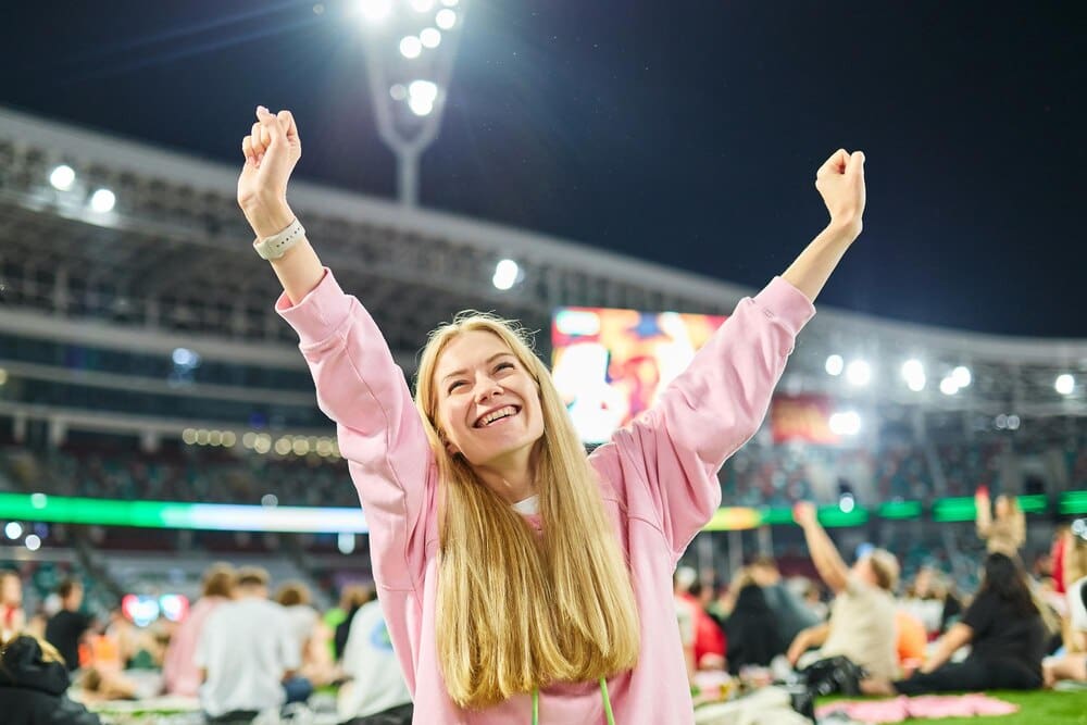A woman sits in a stadium, watching a match broadcast on her laptop.
