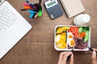 Woman at a desk enjoys a healthy breakfast from a box containing rice berry and a boiled egg.