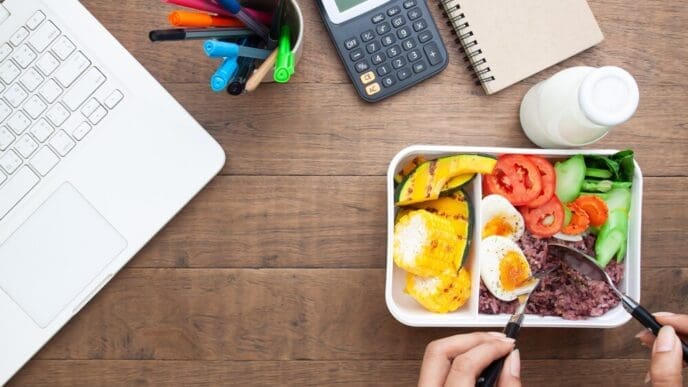 Woman at a desk enjoys a healthy breakfast from a box containing rice berry and a boiled egg.