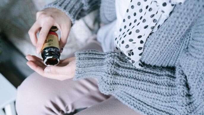 A woman holds a bottle of paint and a sweater with a white polka dot pattern.