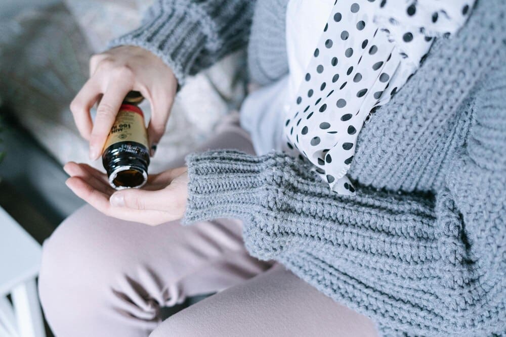 A woman holds a bottle of paint and a sweater with a white polka dot pattern.