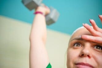 A woman in workout attire lifts a dumbbell, demonstrating focus and determination while exercising in a well-lit room.