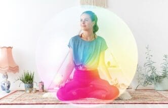 A woman in athletic wear meditates in the lotus position on a yoga mat in a studio.