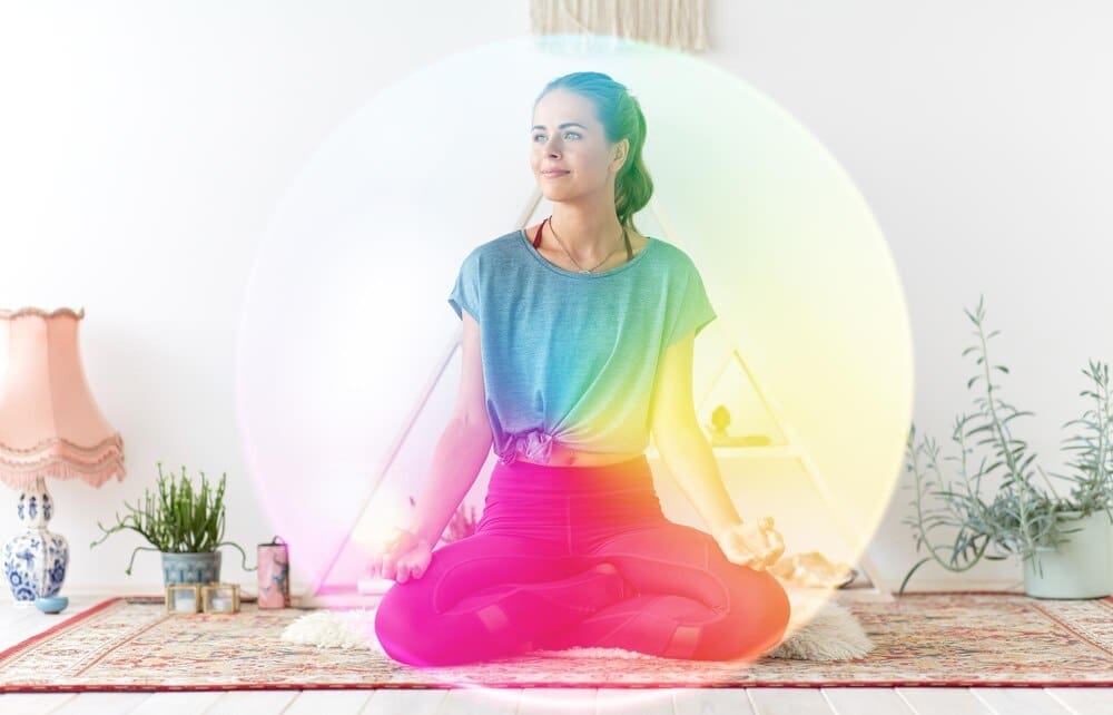 A woman in athletic wear meditates in the lotus position on a yoga mat in a studio.