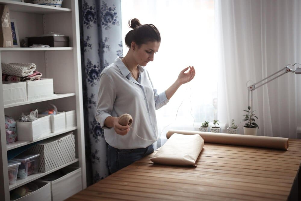 A woman wraps a handicraft item in brown craft paper, likely for shipping or gifting.