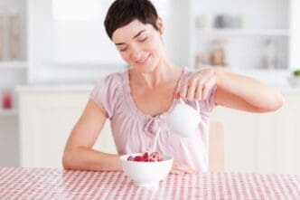 A woman pours a stream of cream over fresh strawberries.