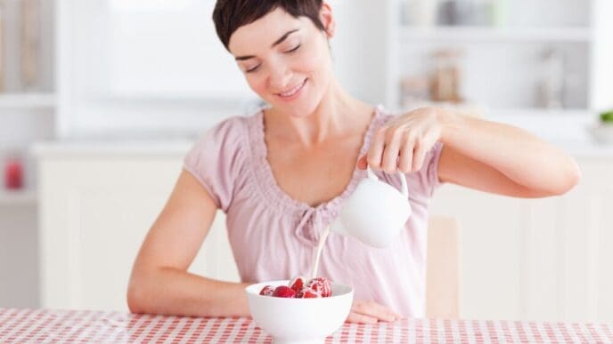 A woman pours a stream of cream over fresh strawberries.