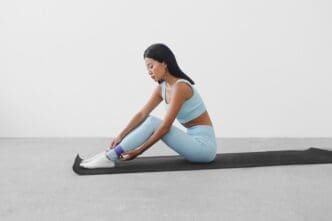 A woman in athletic wear practices a sport on a black yoga mat.