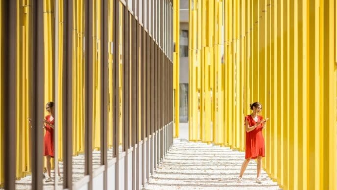 A woman in a red dress stands in front of a modern yellow building, part of an abstract geometric composition.