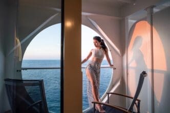 A woman relaxes on a cruise ship balcony, looking out at the ocean.