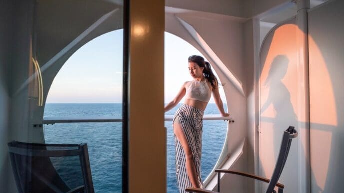 A woman relaxes on a cruise ship balcony, looking out at the ocean.