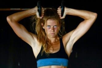 A woman with long hair exercises by holding dumbbells in both hands.