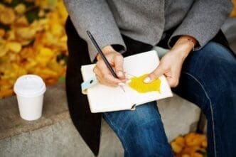 Close-up of a woman's hands holding a paper notebook and pencil, writing or sketching.