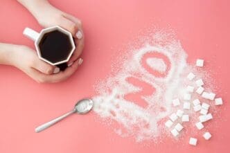 Flat lay of a "No" made of sugar next to a cup of coffee on a pink background.