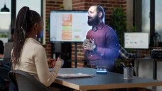 An African American employee watches an augmented reality training video, visualizing a hologram manager explaining how to solve tasks at an innovative office desk computer.
