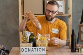 A smiling male volunteer collects a donation box in an office, representing charity work and volunteering.
