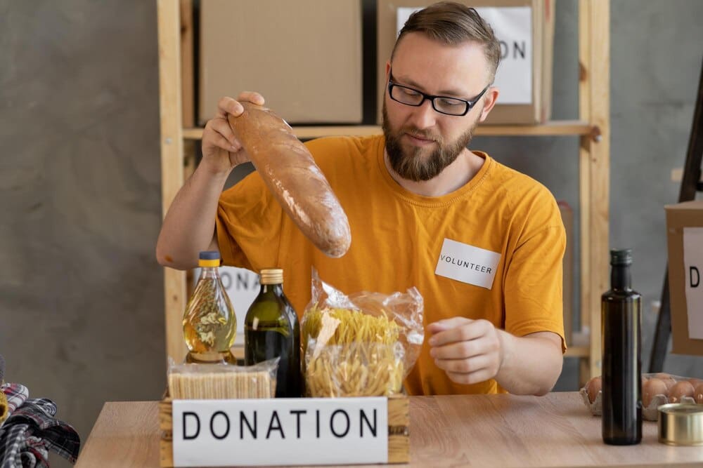A smiling male volunteer collects a donation box in an office, representing charity work and volunteering.