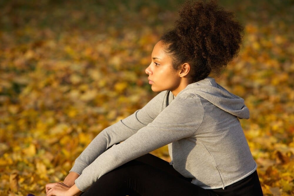 A young African American woman in athletic wear rests outdoors.