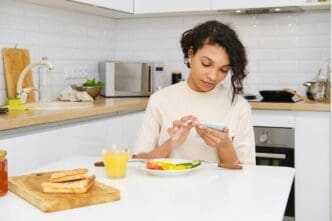 Young Black woman reads a message on her phone while eating breakfast.