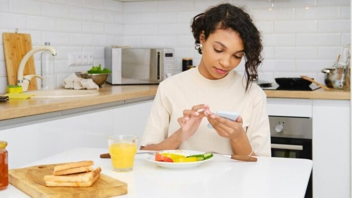 Young Black woman reads a message on her phone while eating breakfast.