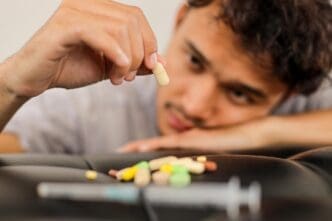 A young Asian man looks distressed, with a pile of pills nearby, suggesting a possible overdose.