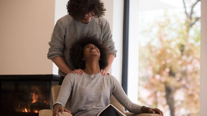 A young multiethnic couple embraces in front of a fireplace while reading a book on an autumn day.