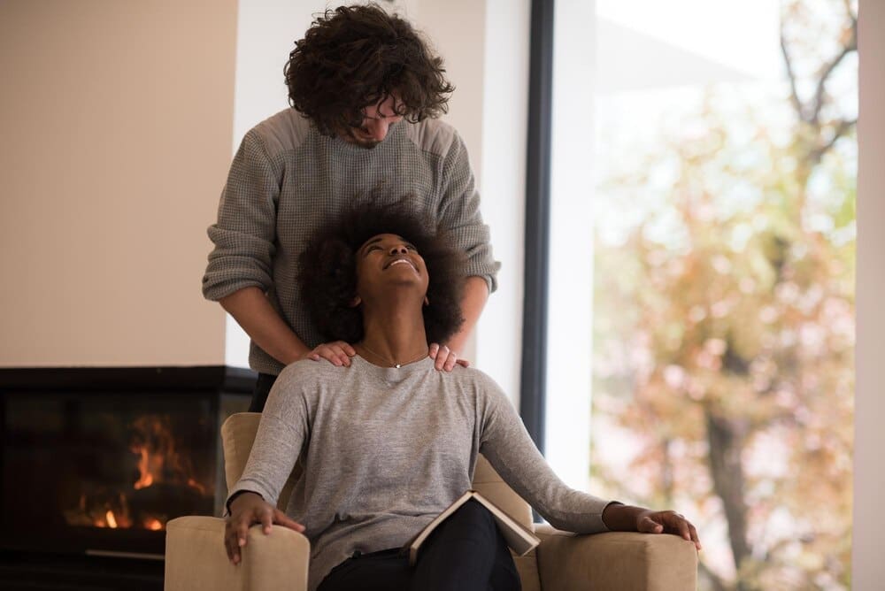 A young multiethnic couple embraces in front of a fireplace while reading a book on an autumn day.
