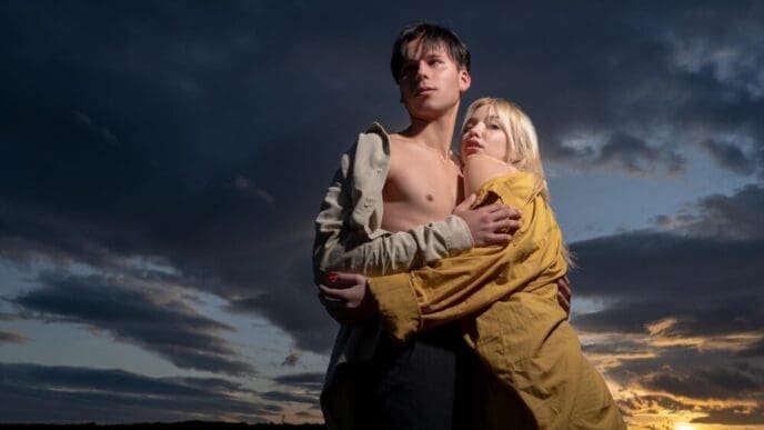A young couple embraces in a loving hug against a dramatic, colorful sky.