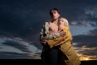 A young couple embraces, silhouetted against a dramatic, colorful sky.