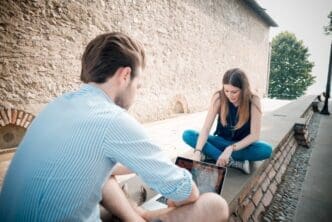 A young couple is multitasking, using a smartphone, tablet, and notebook simultaneously.