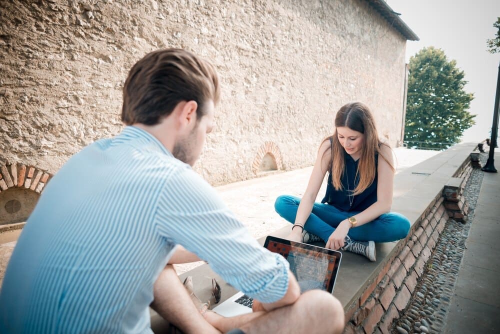 A young couple is multitasking, using a smartphone, tablet, and notebook simultaneously.