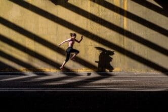 A young, blonde woman in athletic clothing jumps in the middle of a street.