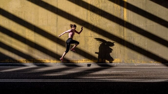 A young, blonde woman in athletic clothing jumps in the middle of a street.