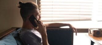 A young man sits at a cafe table, talking on a mobile phone.