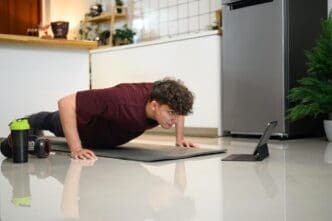Young man in workout clothes doing push-ups while watching a fitness video on a tablet.