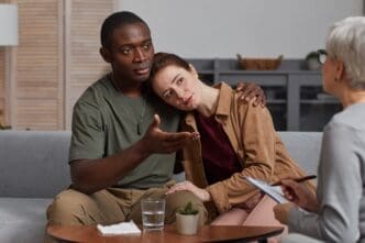 A young multiethnic couple sits together, supporting each other during a consultation with a psychologist.