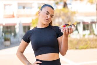 A young brunette woman with a sad expression holds a bowl of fruit outdoors.