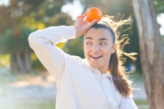A young brunette woman smiles while holding a bright orange.