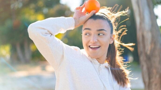 A young brunette woman smiles while holding a bright orange.