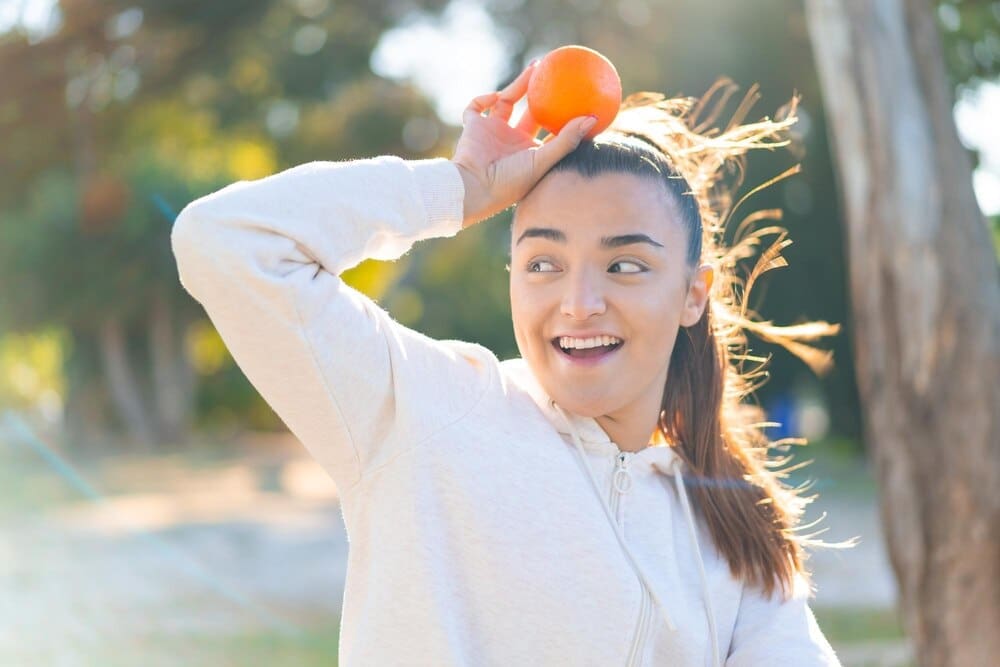 A young brunette woman smiles while holding a bright orange.