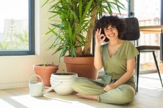 A young woman waters indoor plants with a watering can in her home.