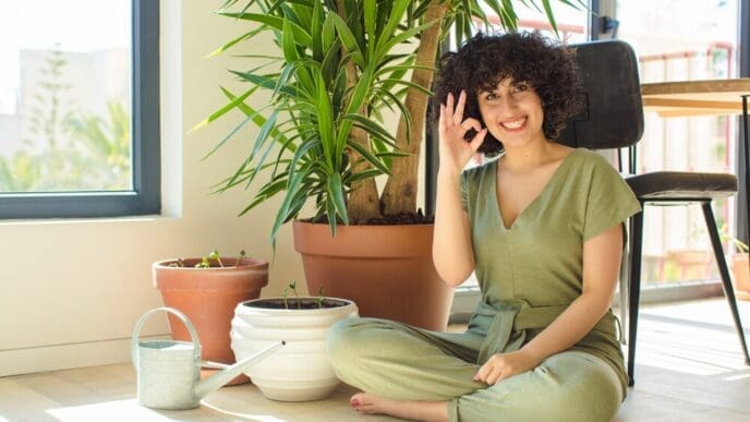 A young woman waters indoor plants with a watering can in her home.