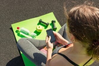 A young woman in athletic wear uses a smartphone while standing on a stadium track.