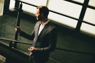 Young businessman in a grey suit stands near a modern building, holding a smartphone.