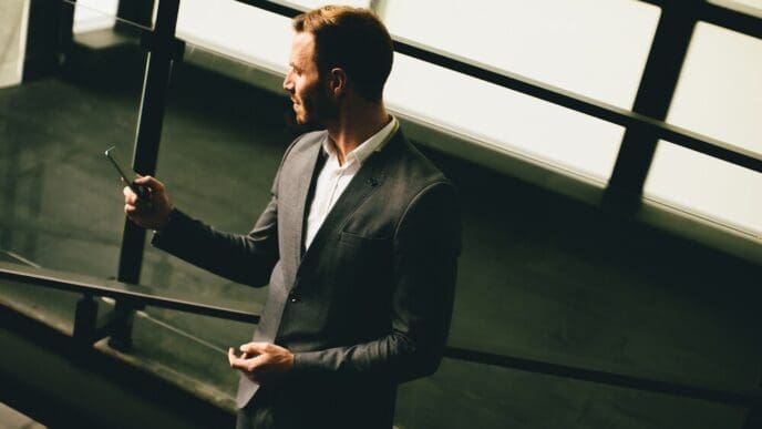 Young businessman in a grey suit stands near a modern building, holding a smartphone.
