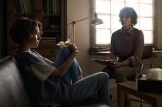 A young woman with a troubled expression sits on a couch facing a psychotherapist.